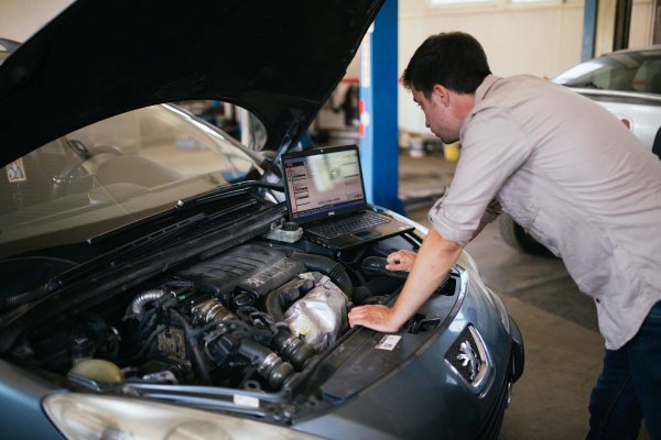 Young mechanic with laptop doing car diagnostic at automobile repair shop closeup