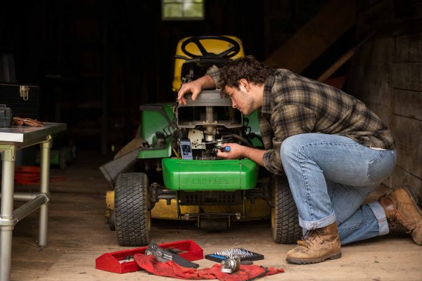 A man repairs a Deere lawnmower with the help of an iFixit guide