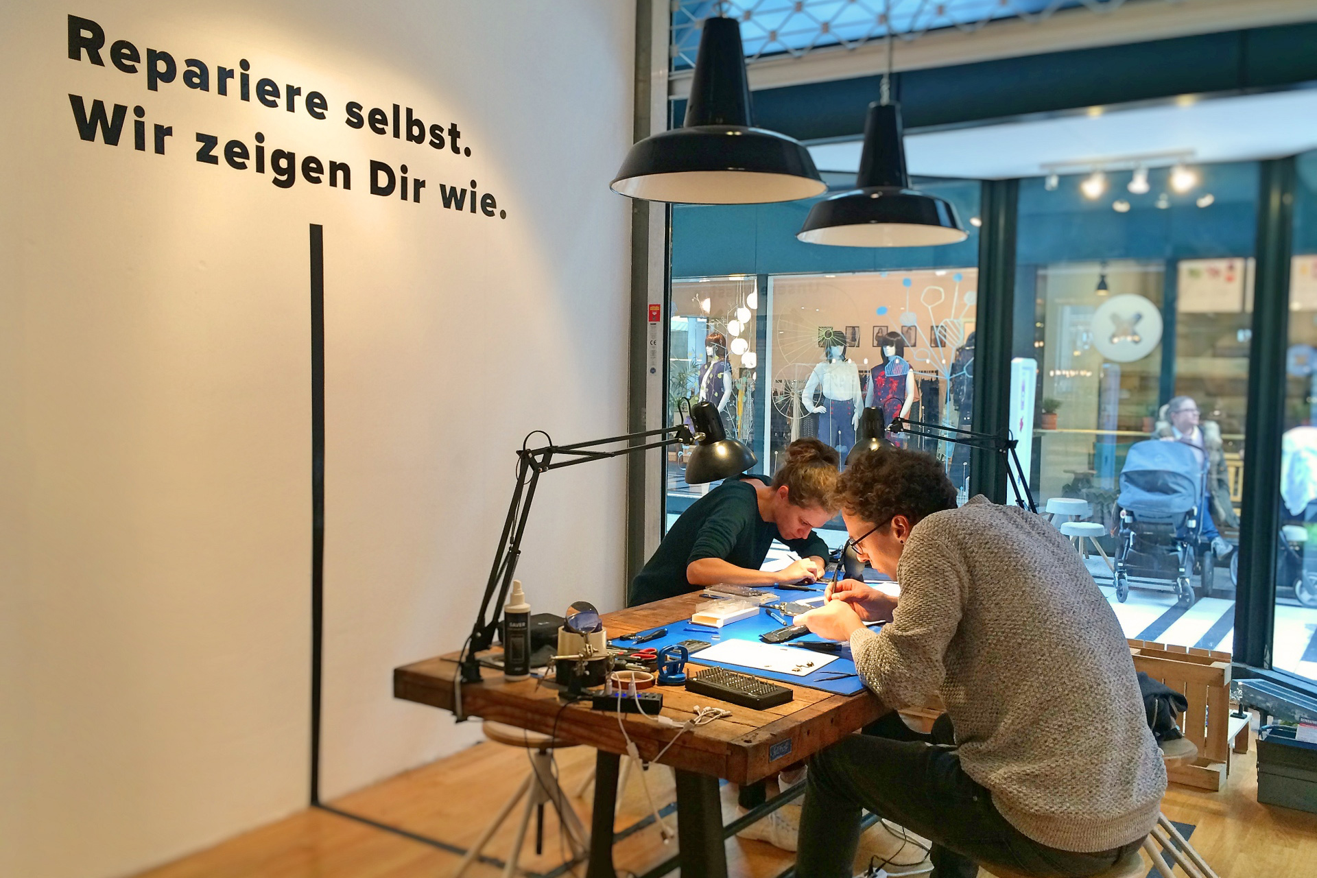 Two people repairing devices in the iFixit pop-up repair shop at the Fluxus Mall