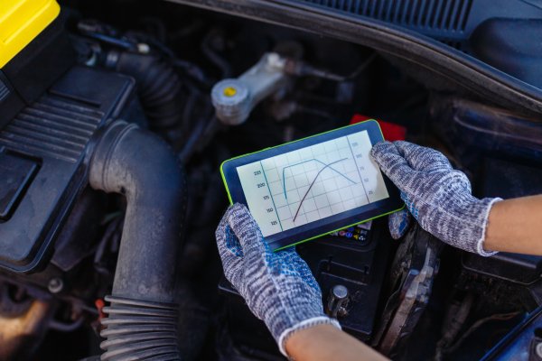 Mechanic's hands holding tablet showing torque graphs over engine